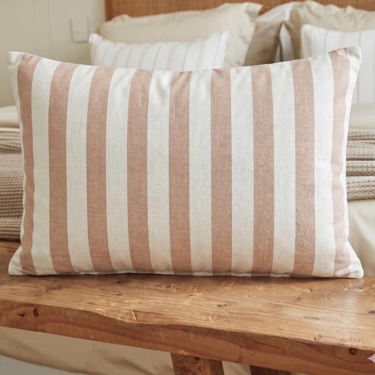 Almohada rectangular con rayas gruesas en salmón y crudo sobre banco de madera-salmón