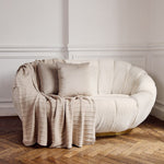 
                    
                      Sofá redondo beige con almohadas y manta a cuadros-
                    
                  