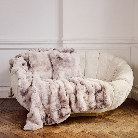 Sofá curvo crema con almohada y manta gris texturizada-gris