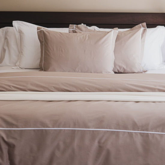 Cama con funda edredón beige y almohadas decorativas en tonos neutros-beige