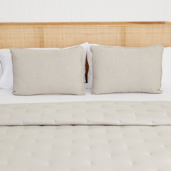 Cama con cubrecama acolchado beige y dos almohadas decorativas a juego-
