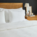 
                    
                      Cama con edredón blanco, almohadas y mesita de noche de madera-
                    
                  