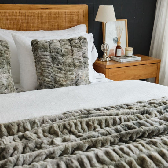 Cama con edredón gris, almohadas texturadas y mesita de noche de madera-