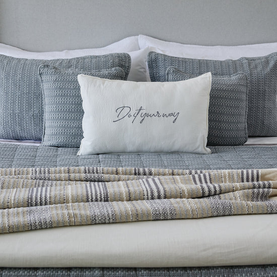 Cama con cubrecama gris, almohadas y cojín blanco con texto-gris