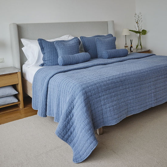 Cama con cubrecama azul acolchado y almohadas decorativas a juego-