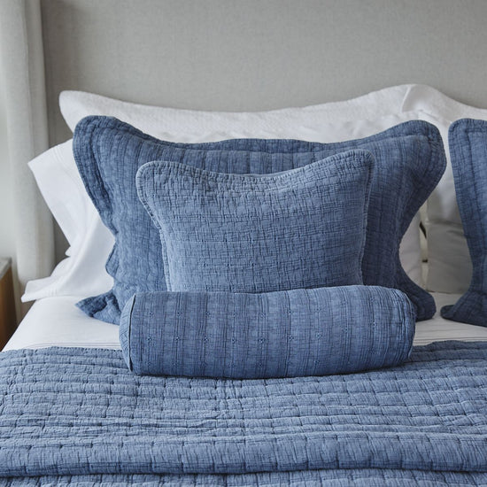 Cubrecama Cardiff azul con almohadas decorativas blancas en cama-