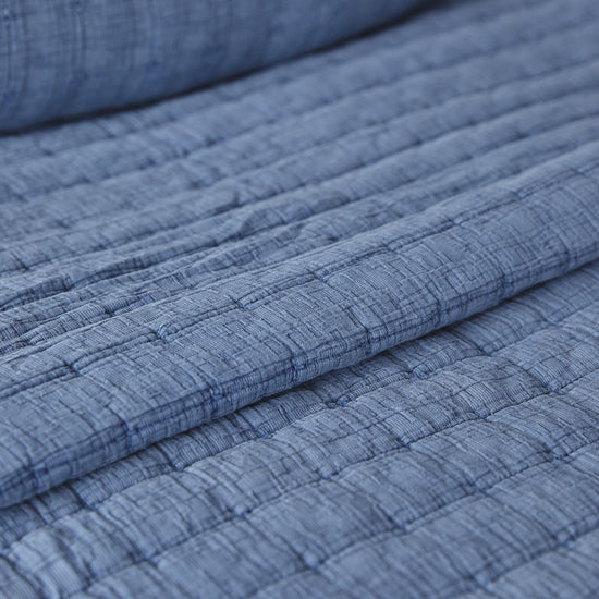 Detalle de textura acolchada de cubrecama azul con líneas horizontales-