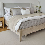 
                    
                      Cama con cubrecama beige, almohadas grises y cabecero tapizado gris-beige
                    
                  