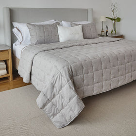 Cubrecama acolchado beige con almohadas decorativas en cama gris-beige