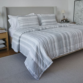 Cama con cubrecama gris a rayas y almohadas a juego-