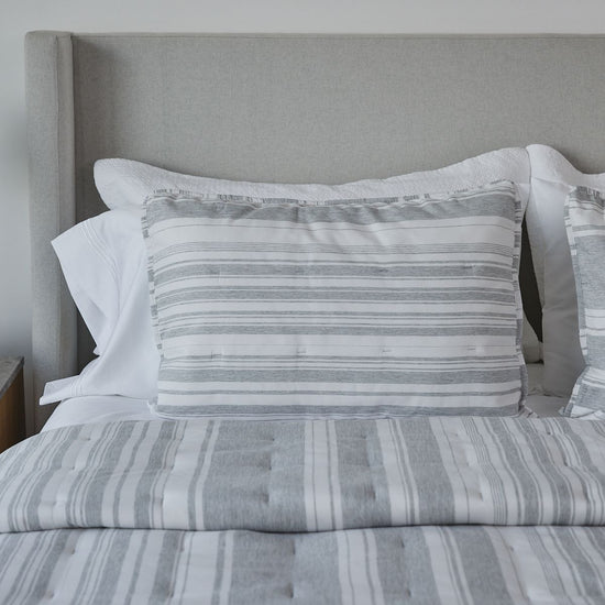 Cama con cubrecama y almohadas de rayas grises y blancas-
