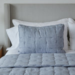 
                    
                      Funda de almohada acolchada gris sobre cama con sábanas blancas-
                    
                  