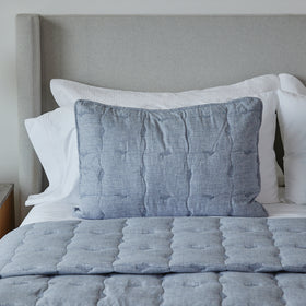 Funda de almohada acolchada gris sobre cama con sábanas blancas-