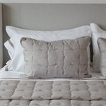 
                    
                      Funda de almohada acolchada beige con detalles en blanco en cama-
                    
                  