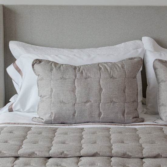 Funda de almohada acolchada beige con detalles en blanco en cama-
