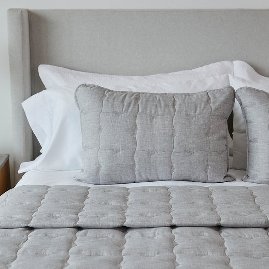 Almohada decorativa gris acolchada sobre cama blanca y beige-