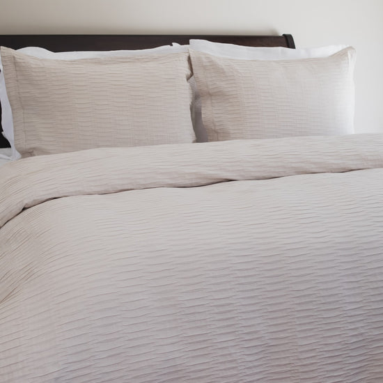 Cama con funda nórdica beige ondulada y almohadas a juego-natural