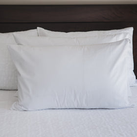 Dos fundas protectoras blancas de almohada sobre cama con cabecero oscuro-blanco