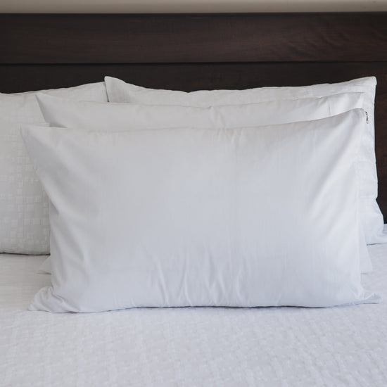 Dos fundas protectoras blancas de almohada sobre cama con cabecero oscuro-blanco