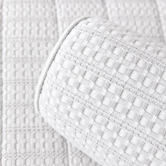 Almohada cilíndrica blanco sobre colcha acolchada de textura cuadriculada-blanco