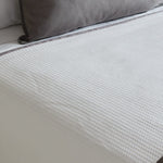 
                    
                      Colcha blanca con textura nido de abeja junto a cojín gris-
                    
                  