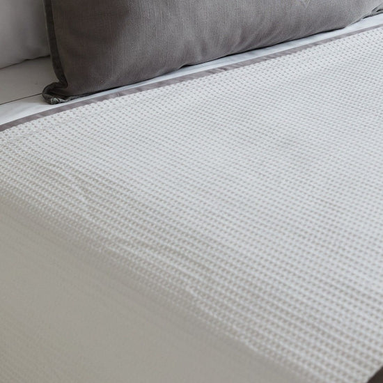 Colcha blanca con textura nido de abeja junto a cojín gris-
