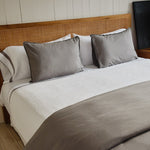 
                    
                      Cama con colcha blanca de nido de abeja y almohadas grises decorativas-
                    
                  