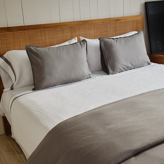 Cama con colcha blanca de nido de abeja y almohadas grises decorativas-