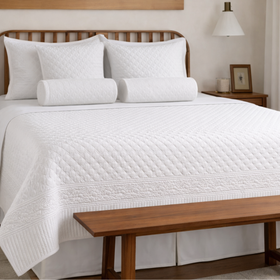 Cubrecama blanco Berna sobre cama con almohadas a juego y banco de madera-blanco