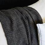 
                    
                      Manta Venecia gris con textura tejida drapeada sobre superficie blanca-gris
                    
                  