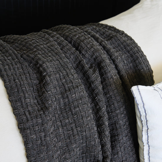 Manta Venecia gris con textura tejida drapeada sobre superficie blanca-gris