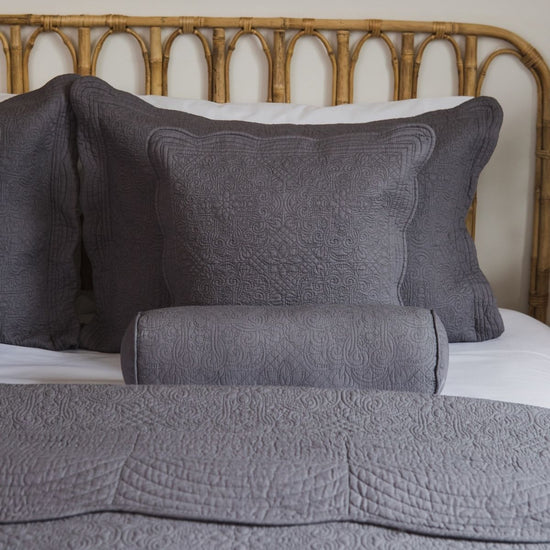 Almohada de barril gris con patrón quilted sobre cama con cabecero de ratán-gris claro