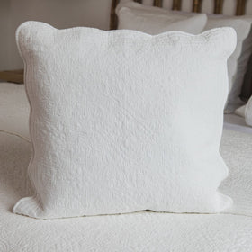 Funda de almohón blanca acolchada con bordes ondulados sobre cama-natural