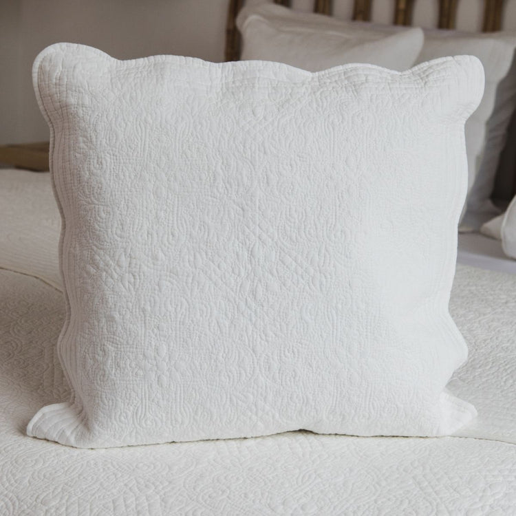 Funda de almohón blanca acolchada con bordes ondulados sobre cama-natural