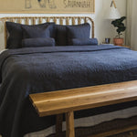 
                    
                      Cama con cubrecama gris oscuro, cabecera ratán y banco madera-gris
                    
                  