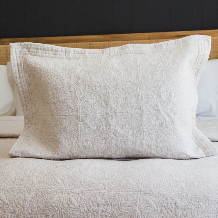 Funda de almohada Amalfi beige con patrón quilted sobre cama-beige