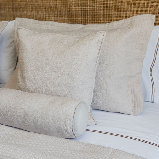 Almohadas beige con patrón quilted en cama con sábanas blancas-beige