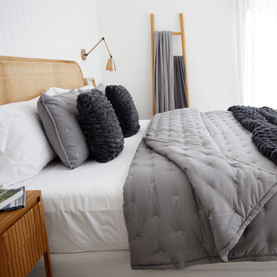 Cama con cubrecama gris, almohadas y textiles de lana natural-gris
