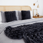 
                    
                      Cama con cubrecama gris, almohadas negras y cabecera de madera natural-gris
                    
                  