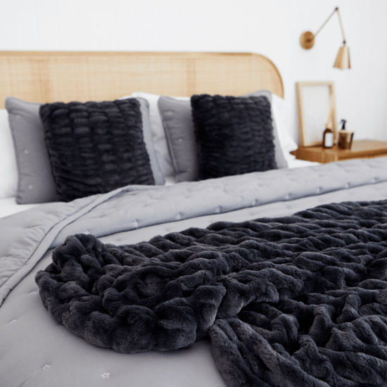 Cama con cubrecama gris, almohadas negras y cabecera de madera natural-gris