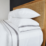 
                    
                      Cama con sábanas blancas, almohadas y aplique gris en cabecera de ratán-gris
                    
                  