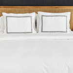 
                    
                      Cama con dos almohadas blancas con ribete gris sobre edredón blanco-gris
                    
                  