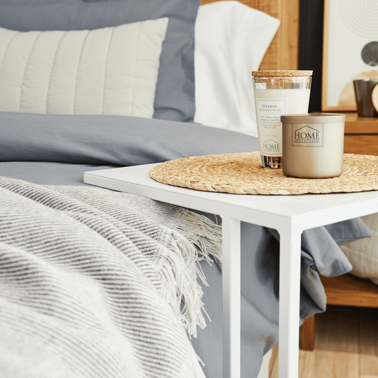 Vela Home Collection sobre mesa junto a cama con almohadas blancas-jengibre
