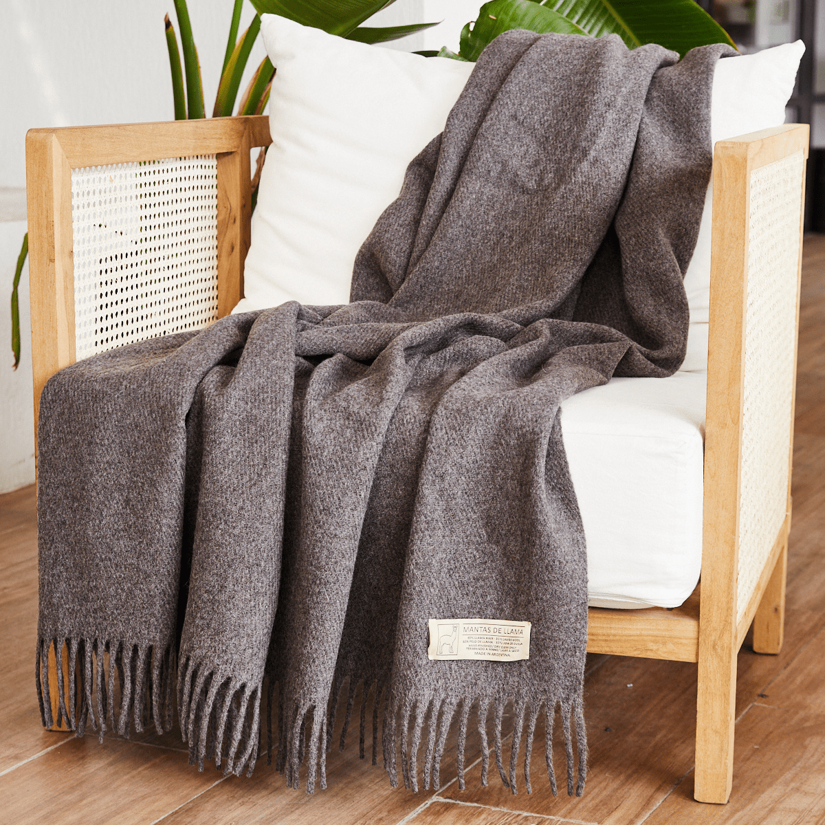 Manta gris de llama draped sobre silla de madera con plantas-gris