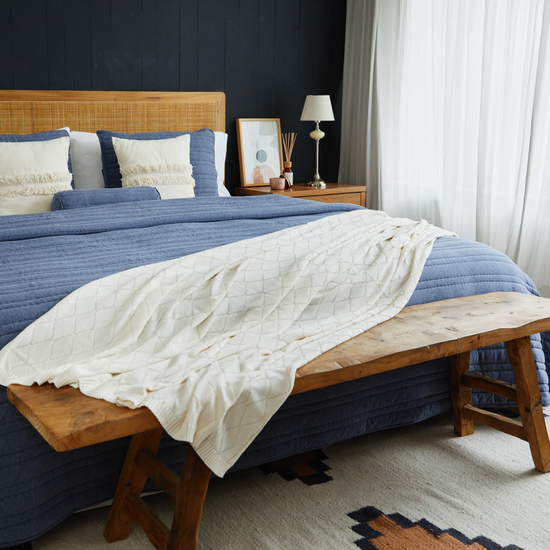 Cubrecama azul sobre cama con almohadas blancas y banco de madera-azul