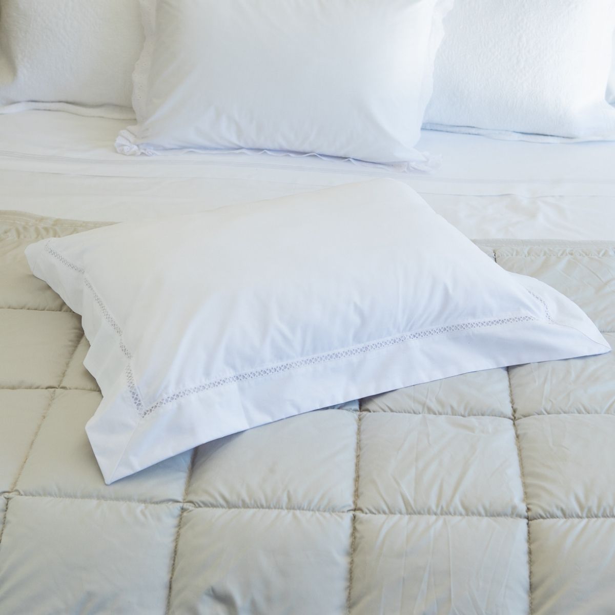 Dos almohadas blancas con detalle de encaje sobre colcha acolchada beige-vainilla