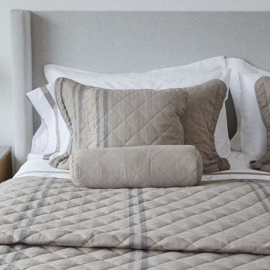 Cama con cubrecama acolchado beige, almohadas y cilindro decorativo-