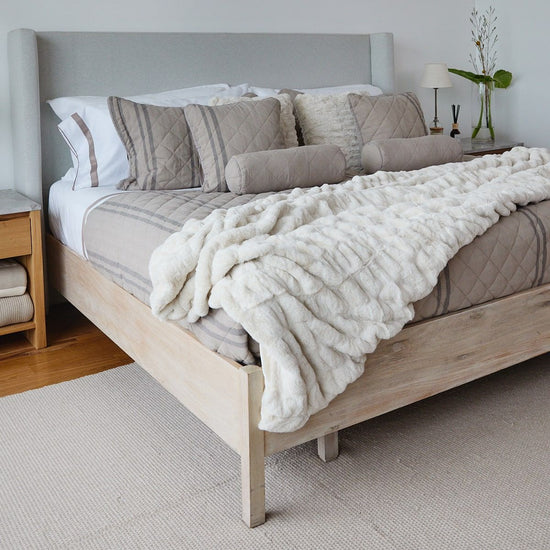 Cama con cubrecama acolchado blanco y almohadas decorativas grises-