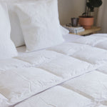 
                    
                      Edredón blanco sintético sobre cama con almohadas y decoración-
                    
                  