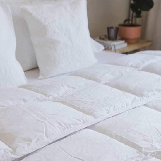 Edredón blanco sintético sobre cama con almohadas y decoración-